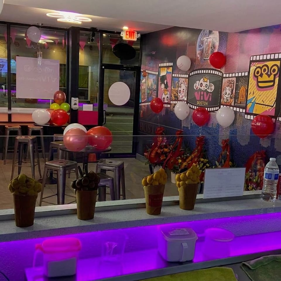 Colorfully decorated restaurant interior with balloons, mural artwork, seating, and a counter displaying dessert cups and beverages.