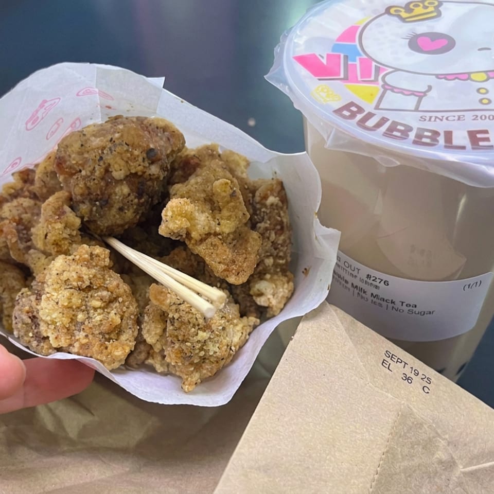 Basket of crispy fried bites with wooden picks beside a sealed cup of milk tea on a restaurant table.