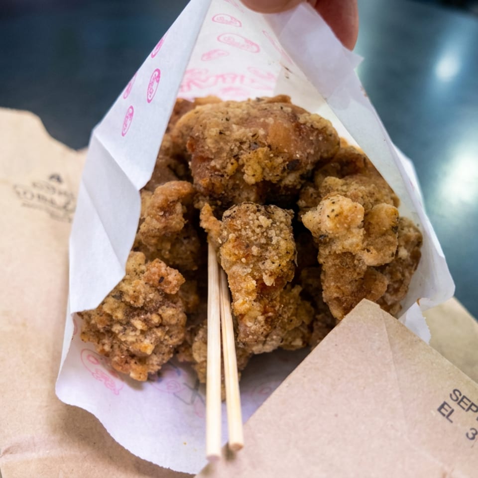 Crispy fried chicken pieces served in branded paper with wooden chopsticks on a dark restaurant table.