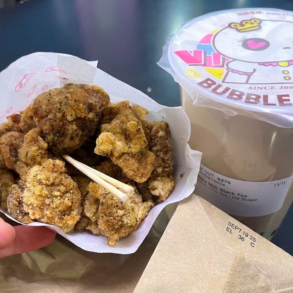 Tray of crispy fried bites with chopsticks beside a sealed cup of Vivi Bubble Tea on a dark table.