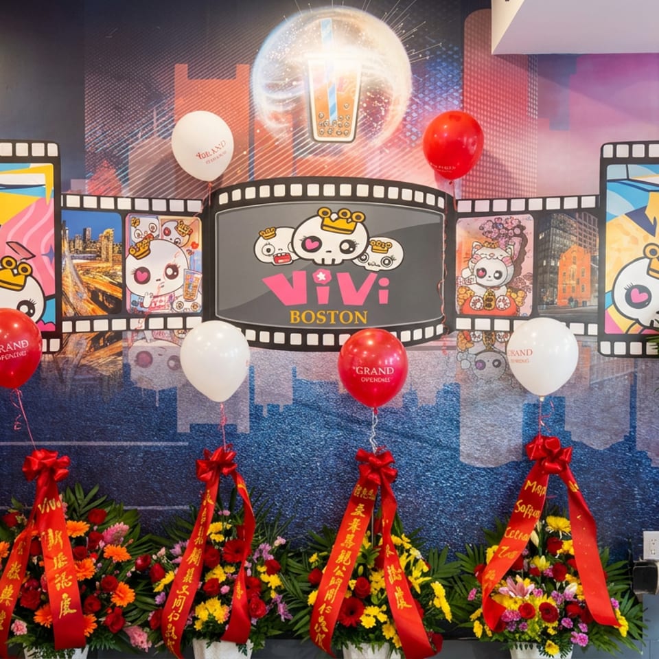 A festive grand-opening display for Vivi Boston features cartoon character artwork, balloons, and colorful floral stands with red ribbons.
