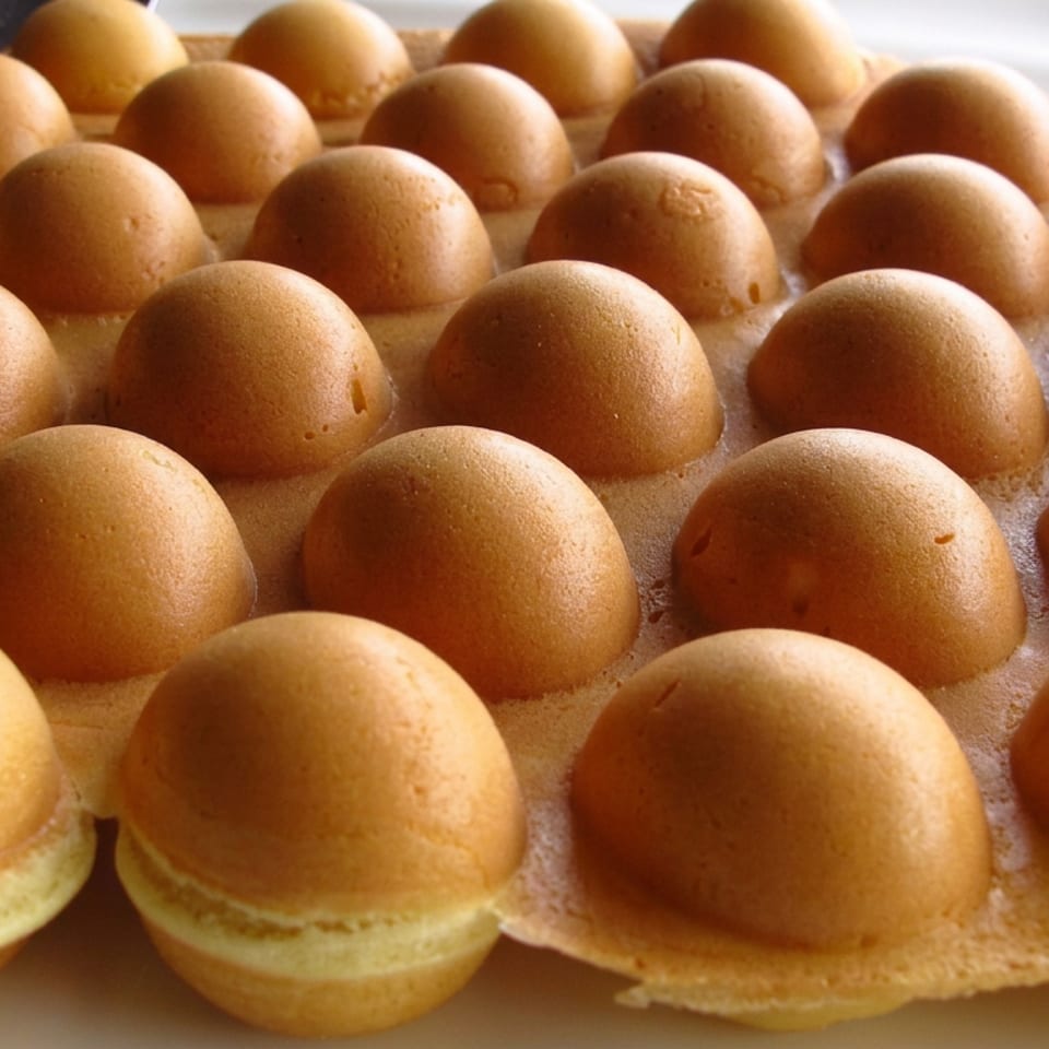 Tray of golden, dome-shaped sponge cakes arranged in rows, with pale filling visible between their layers.
