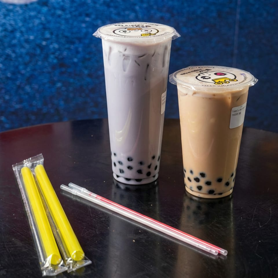 Two sealed cups of milk tea with black tapioca pearls and colorful straws sit on a dark table.