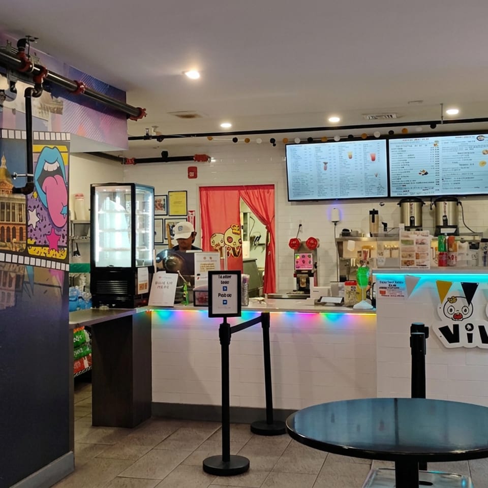 Colorful Vivi bubble tea counter with digital menus, self-service kiosk, arcade prize machine, and playful cartoon murals.